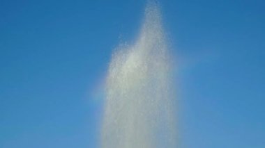 Top of fountain against blue sky. Many drops of water fly in different directions.