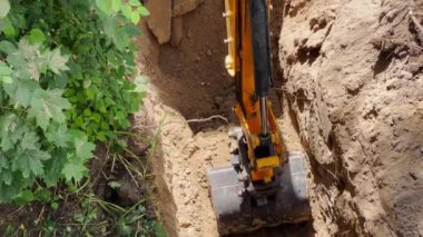 Digging hole in ground with excavator. Attention is focused on bucket of excavator removing part of soil.