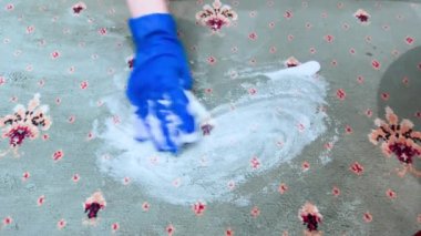 Mavi eldivenli kadın eli bol köpüklü deterjanla halıyı yıkıyor..