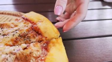 Kadının eli, ahşap tepside uzanan sıcak kokulu pizzayı kırar. Acelesi olmayan kamera hareketi.