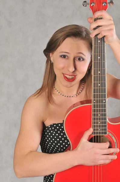 Chica emocional con una guitarra roja, sobre un fondo gris — Foto de Stock