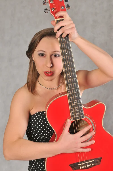 Эмоциональная девушка с красной гитарой, на сером фоне — стоковое фото