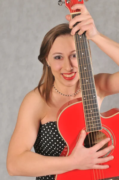 Emotionales Mädchen mit roter Gitarre auf grauem Hintergrund — Stockfoto