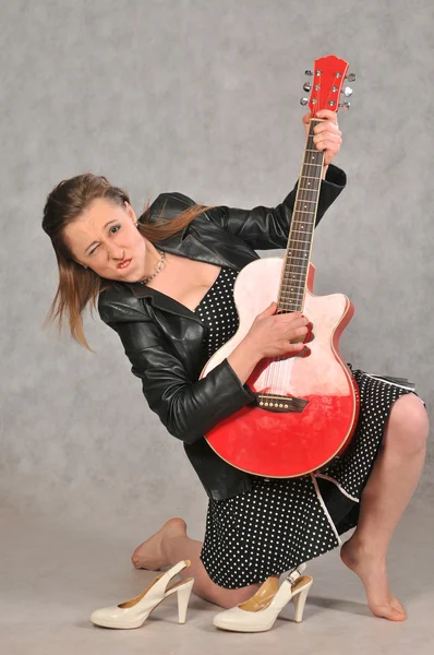 Ragazza emotiva con una chitarra rossa, su sfondo grigio — Foto Stock