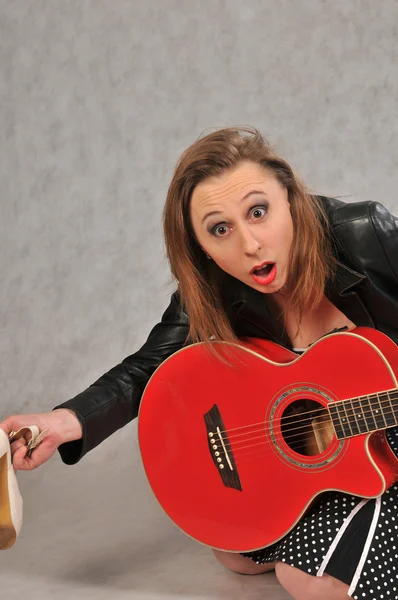 Emotional girl with a red guitar, on a grey background — Stock Photo, Image