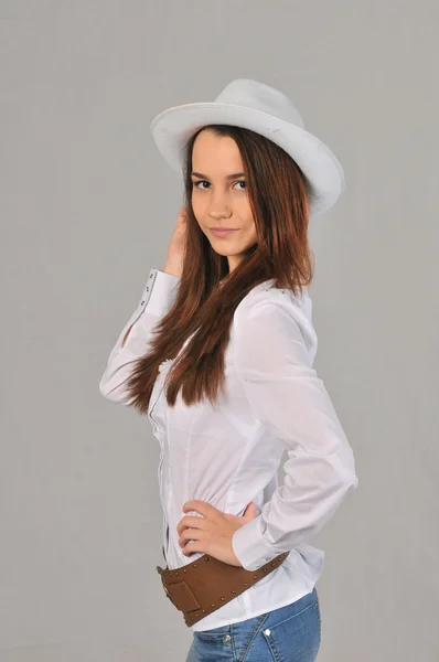 Ragazza piegare la schiena in una camicetta bianca e jeans con una mano che tiene il cappello bianco sulla testa — Foto Stock