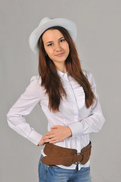 Una ragazza con un cappello bianco, camicia bianca, jeans e cintura da cowboy tiene la mano destra sulla cintura — Foto Stock