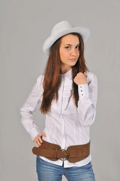 A girl in a white hat, white shirt, jeans and cowboy belt holding his right hand on the waist and the other pulls hair — Stock Photo, Image