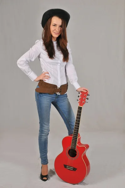 Young girl standing in a blouse with short sleeves, keeping the left hand along the body, and the right is based on the neck of the red guitar — Stock Photo, Image