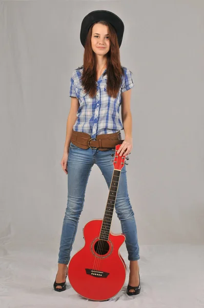 Junges Mädchen in einer Bluse mit kurzen Ärmeln, die rechte Hand am Körper entlang, die linke am Hals der roten Gitarre — Stockfoto