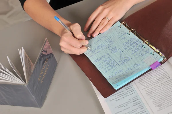 Den unga kvinnans hand skriver anteckningar på skrivbordet Royaltyfria Stockfoton