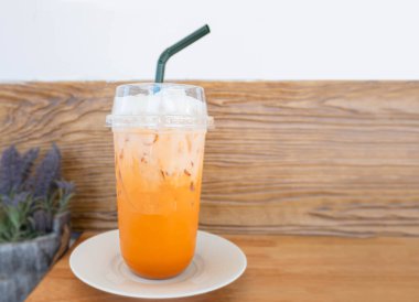 Ahşap masa barı ve kafe kahve arka planında plastik bir bardak Thai portakalı çayı. İçkiye hazır konsepti kaldırmak için.
