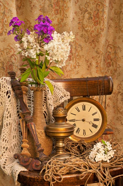 Still life with phlox bouquet in a vintage vase on the old chair with antique clock and oil lamp — Stock Photo, Image