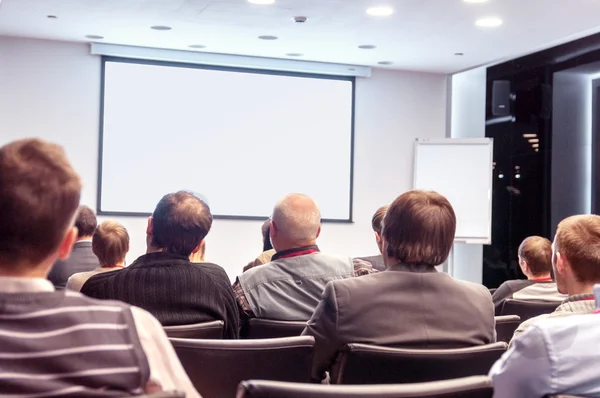 Menschen, die hinten auf der Konferenz sitzen und auf den Bildschirm schauen — Stockfoto