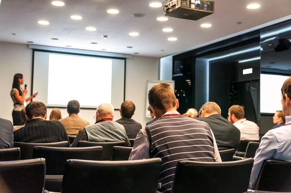 Conferenza d'affari. persone sedute dietro e donne che parlano sullo schermo — Foto Stock