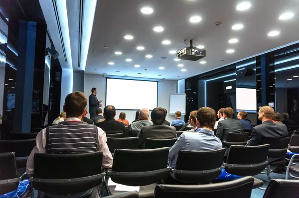 Personas sentadas en la parte trasera de la conferencia de negocios y altavoz en la pantalla blanca — Foto de Stock