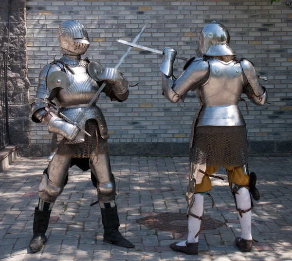 Two knights in the ancient metal armor standing near the stone wall Stock Image