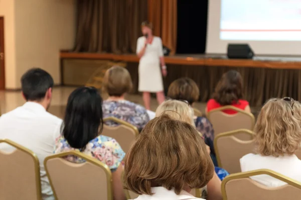 Business conference - people sitting rare and speaker near the screen — Stock Photo, Image