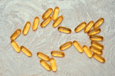 Omega3 kapsülleri, çimento arka planında balık şeklinde siluetler. EPA ve DHA vücudumuzun günlük olarak ihtiyaç duyduğu temel yağ maddeleridir..