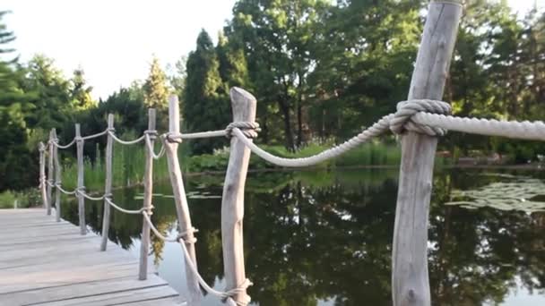 Old wooden walking bridge across lagoon to green garden. — Stock Video