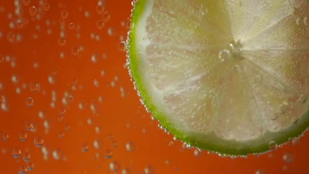 Limette in Sodawasser auf orangefarbenem Hintergrund — Stockvideo