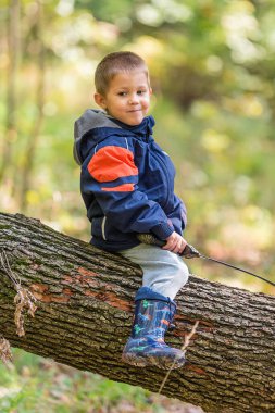 Genç çocuk devrilmiş ağaç gövdesinde oturuyor ve kılıçla oynuyor.