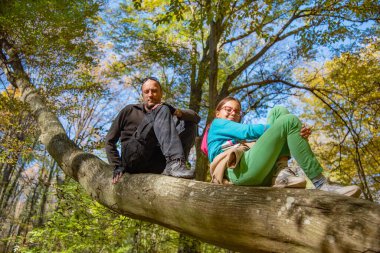 Baba ve kızı ağaca tırmandı. Sonbahar ormanında bir ağaçta oturan aile.