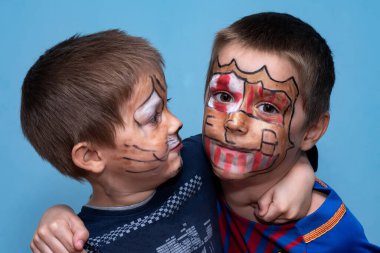 Kardeşler sarılır ve kameraya bakar. Yüz boyalı çocuklar.