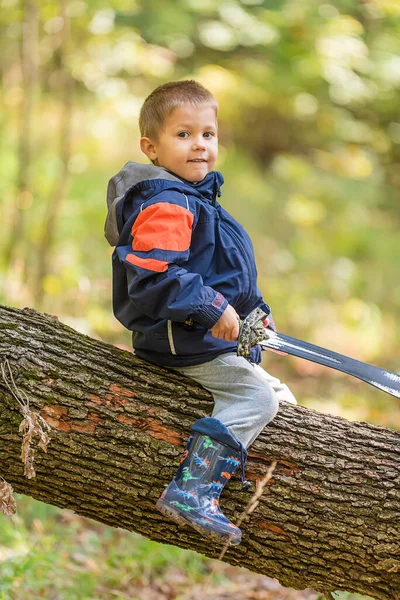 Genç çocuk devrilmiş ağaç gövdesinde oturuyor ve kılıçla oynuyor.