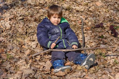 Çocuk ormanda bir yaprağın üzerinde yatıyor. Sarı sonbahar yapraklı küçük çocuk parkta