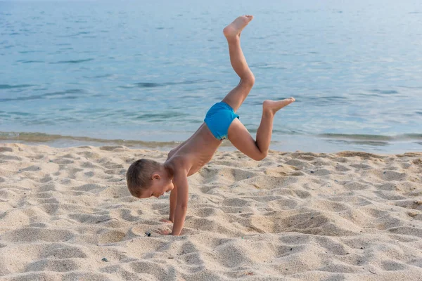 ビーチの子供はスポーツをし 海を背景に体操を行います 子供は海岸に手を出す — ストック写真