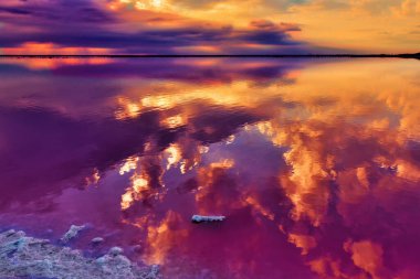 Gökyüzünün bir kısmı koyu yoğun bulutlarla kaplıdır. Güneş onların ardından doğar ve gökyüzünü aydınlatır. Gökyüzü bulutlarla çevrili, tuzlu gölün pembe sularında.