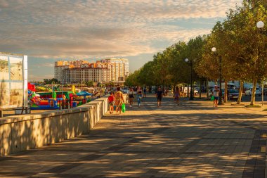 Akşam vakti, insanlar sette yürüyor ve şehir plajında dinleniyorlar.