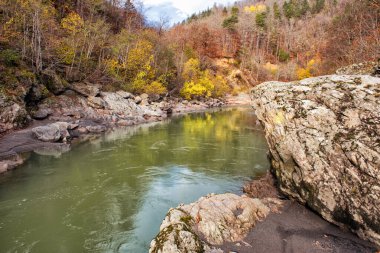 Nehrin yavaş akışı kayalık kıyılarda, karışık bir ormanın büyüdüğü yerde, ağaçlardaki yapraklar sonbahar renklerinde boyanır.