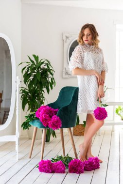 Beyaz elbiseli bir kadın stüdyoda beyaz bir odada, aşağıya bakıyor. Üzgün ruh hali, sakinlik ve kendini dizginleme.