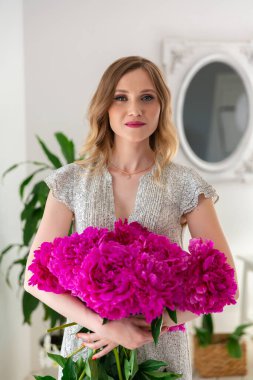 İş kadını çiçekçi kadın atölyede çiçek buketi yapıyor. Girişimci elinde bir buket pembe şakayık tutuyor.