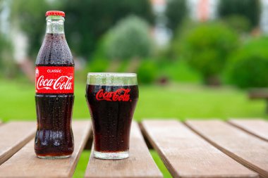Krasnoyarsk, Rusya - 07.14.2020: tahta kalasların üzerinde duran cam Coca-Cola şişesi. Tazeleyici içecek. Susuzluk giderici. Metin için yer.
