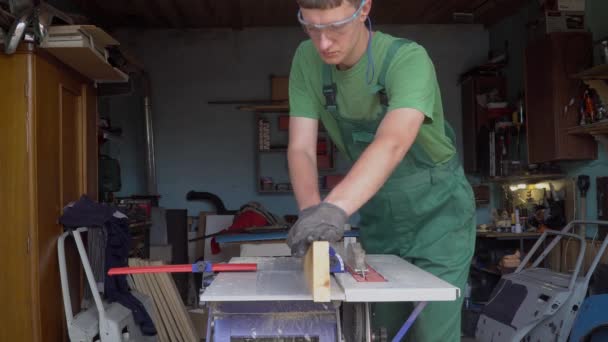 Ξυλουργός σε προστατευτικά γάντια και υαλοπίνακες χειρίζεται μια ξύλινη σανίδα εργασίες για planing μηχάνημα στο εργαστήριο. — Αρχείο Βίντεο