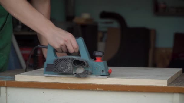 ワークショップで木製の板の上の電気プランターで作業カーペンター。職人がテーブルを作る — ストック動画