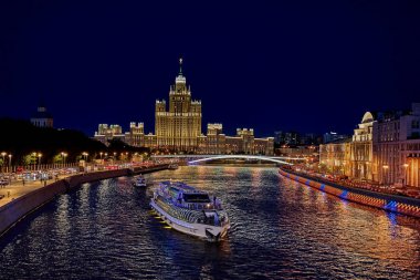 Moskova, 23 Haziran 2021: Gece şehri manzarası, arka planda Moskova nehrinde bir eğlence teknesi yüzüyor Stalinist bir gökdelen.