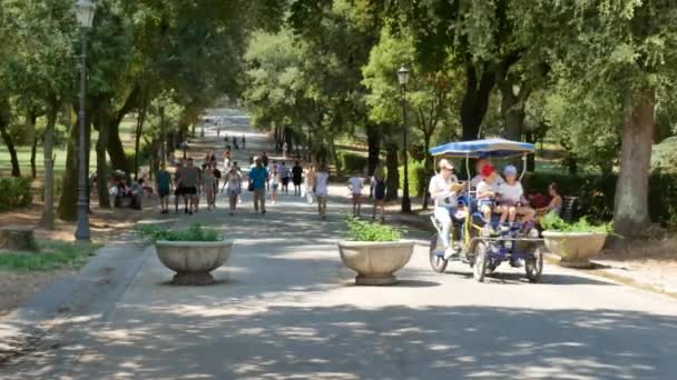 Família de bicicleta através da pista frondosa no Villa Borghese jardins - 4K, Rastreamento tiro, Editorial — Vídeo de Stock