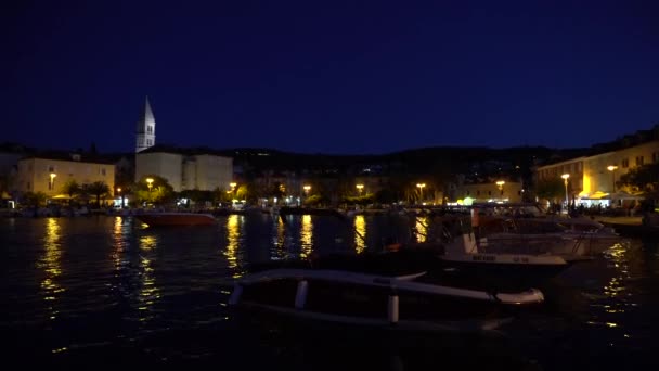 Passeio marítimo iluminado e barcos em pequena cidade Supetar na Croácia à noite - 4K, Wide shot, Handheld — Vídeo de Stock