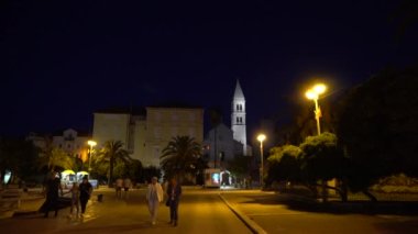 Akşamları Hırvatistan 'ın küçük Supetar kasabasında Aziz Peter Kilisesi yakınlarındaki aydınlık sokaktaki insanlar - editör, 4K, geniş çekim