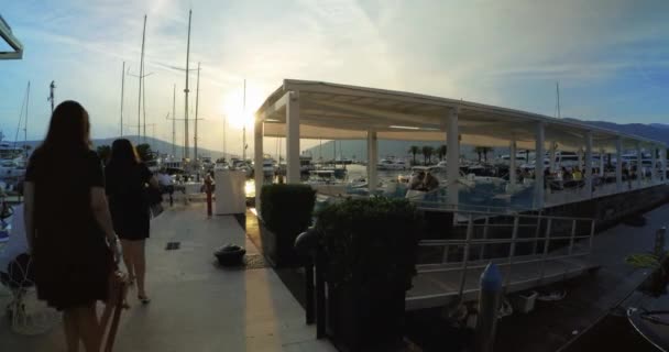 Two women walk near the restaurant terrace at sunset in Porto Montenegro, Tivat - Editorial, DCI 4K, Ultra Wide, Handheld — Stock video