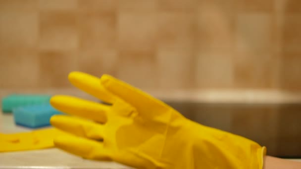 Kvinna sätter gul rengöringshandske, suddig induktion spishäll och blå rengöringssvampar på bakgrunden - 4K, Närbild — Stockvideo