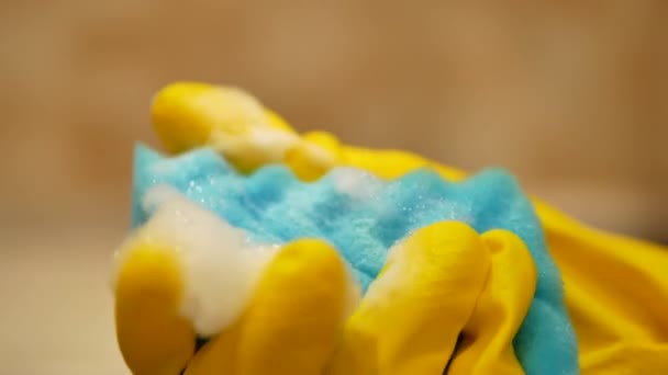 Hand in Hand in gelbem Putzhandschuh hält blauen Schaumschwamm und beginnt dann, Kochfeld auf verschwommenem Hintergrund zu reinigen - 4K, Nahaufnahme — Stockvideo