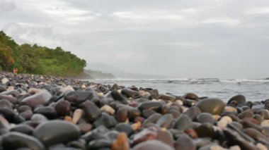Güneş doğarken deniz kıyısında çakıl taşları ve Amed, Bali 'de deniz dalgaları - 4K, ultra geniş çekim, Saha Sığ Derinliği