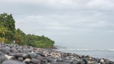 Çakıl taşlı plaj, okyanus dalgaları ve güneş doğarken palmiye ağaçları ve Amed, Bali 'de - 4K, Sığ Alan Derinliği, Düşük açı, Ses