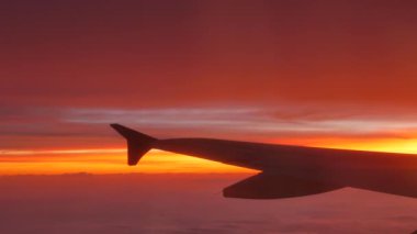 Gün batımında bulutların üzerinden uçak kanadına bak. 4K, el bilgisayarı. Ses içerir