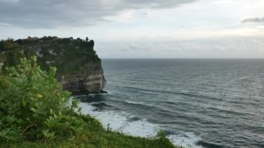 Bali, INDONEZYA - 22 Ocak 2018: Yeşil Uluwatu tapınağı uçurumu ve Hint Okyanusu dalgaları rüzgarlı günbatımında kıyıya vuruyor, Bali. 4K, geniş açı
